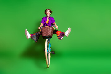 Poster - Photo of funny screaming young woman wear purple shirt and brown bob haircut riding bicycle legs up isolated on green color background