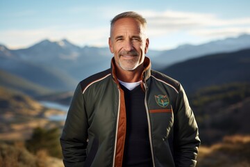 Wall Mural - Portrait of a happy man in his 50s sporting a stylish varsity jacket in front of panoramic mountain vista