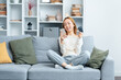 Happy Young Woman Using Credit Card, Smiling As She Decides On Financial Choices On Comfortable Living Room Sofa, Home Shopping Concept