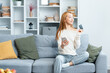 Young Woman Using Credit Card On Couch, Appearing Content And Thoughtful, Modern Home Setting With Stylish Furniture, Concept Of Online Shopping And Decision Making