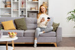 Young Woman Relaxing On Sofa With Smartphone And Credit Card, Comfortably Dressed In Casual Home Environment, Displaying Modern Lifestyle And Online Shopping.