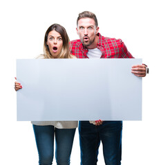 Canvas Print - Young couple together holding blank banner over isolated background scared in shock with a surprise face, afraid and excited with fear expression