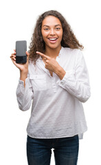 Canvas Print - Young hispanic woman using smartphone very happy pointing with hand and finger