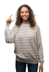 Wall Mural - Beautiful young hispanic woman wearing stripes sweater smiling and confident gesturing with hand doing size sign with fingers while looking and the camera. Measure concept.