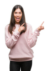 Wall Mural - Young beautiful hispanic woman wearing a sweater smiling and looking at the camera pointing with two hands and fingers to the side.