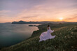 A woman in a white dress is walking on a grassy hill overlooking a body of water