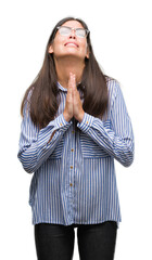 Poster - Young beautiful hispanic business woman begging and praying with hands together with hope expression on face very emotional and worried. Asking for forgiveness. Religion concept.