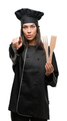 Wall Mural - Young hispanic cook woman wearing chef uniform pointing with finger to the camera and to you, hand sign, positive and confident gesture from the front