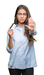 Sticker - Young arab woman holding credit card over isolated background with open hand doing stop sign with serious and confident expression, defense gesture