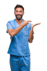 Canvas Print - Adult hispanic doctor or surgeon man over isolated background amazed and smiling to the camera while presenting with hand and pointing with finger.