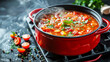 Steaming vegetable soup in a red pan surrounded by fresh ingredients on a kitchen stove