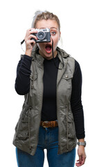 Wall Mural - Young blonde woman taking pictures using vintage camera over isolated background scared in shock with a surprise face, afraid and excited with fear expression