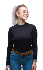 Poster - Young blonde woman wearing glasses over isolated background looking away to side with smile on face, natural expression. Laughing confident.