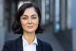 © Tetiana - Close-up photo of a smiling young woman in a business suit standing outside a building and looking at the camera