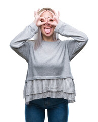 Wall Mural - Young blonde woman over isolated background doing ok gesture like binoculars sticking tongue out, eyes looking through fingers. Crazy expression.