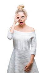 Poster - Young beautiful blonde and blue eyes woman over isolated background doing ok gesture shocked with surprised face, eye looking through fingers. Unbelieving expression.