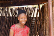 village young african girl with red dress standing i standing at the entrance of the shack, township village in south africa