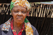 portrait of a village senior african woman standing in in the yard fence on the background
