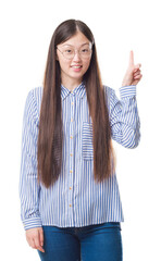 Wall Mural - Young Chinese business woman over isolated background wearing glasses surprised with an idea or question pointing finger with happy face, number one