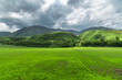 Green field against a background of green hills. Sky with clouds. Journey into the wild.