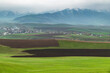 Plowed fields on green hills against the backdrop of misty mountains. Spring in Kyrgyzstan.