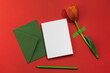 Red tulip taped on a red background, an envelope and a blank white card and a green pencil. Greeting card, invitation with copy space.