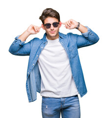 Young handsome man wearing sunglasses over isolated background Smiling pulling ears with fingers, funny gesture. Audition problem