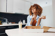 Curly haired woman enjoying pizza while standing in kitchen holding pizza box