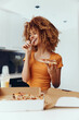 Young woman with curly hair enjoying a slice of pizza in front of a opened pizza box