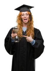 Canvas Print - Young redhead student woman wearing graduated uniform holding hourglass very happy pointing with hand and finger