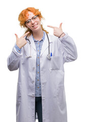 Sticker - Young redhead woman wearing doctor uniform smiling confident showing and pointing with fingers teeth and mouth. Health concept.