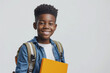 © Volodymyr - Studio portrait of a cheerful African American boy with a backpack standing isolated on a light background, gripping a textbook