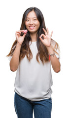 Canvas Print - Young asian woman eating pink macaron sweet over isolated background doing ok sign with fingers, excellent symbol