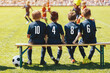 Substitute Players in Soccer Team Sitting on the Bench. Multiethnic Group of Children in Sports Team Support a Soccer Team in a Game. School Football Team Members in Blue Jerseys With Numbers
