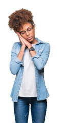 Wall Mural - Beautiful young african american woman wearing glasses over isolated background sleeping tired dreaming and posing with hands together while smiling with closed eyes.