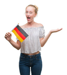 Sticker - Blonde teenager woman holding flag of Germany very happy and excited, winner expression celebrating victory screaming with big smile and raised hands