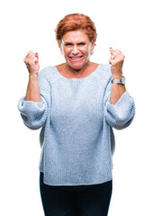 Poster - Atrractive senior caucasian redhead woman wearing winter sweater over isolated background excited for success with arms raised celebrating victory smiling. Winner concept.