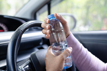 Asian woman driver holding bottle for drink water while driving a car. Plastic hot water bottle cause fire.