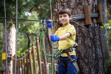 Wall Mural - Strong excited young boy playing outdoors in rope park. Caucasian child dressed in casual clothes and sneakers at warm sunny day. Active leisure time with children concept