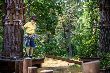 Wall Mural - Strong excited young boy playing outdoors in rope park. Caucasian child dressed in casual clothes and sneakers at warm sunny day. Active leisure time with children concept