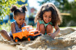 Two girls having fun playing together with toy truck in sand pit