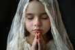 Young girl in her holy communion outfit with white veil, praying.