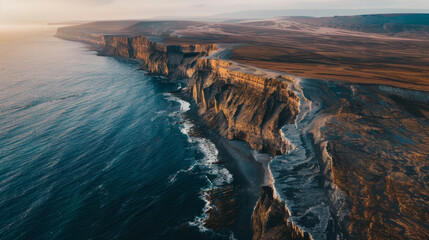 Wall Mural - Drone perspective of a coastline where cliffs meet the ocean, capturing the dramatic interaction between land and sea at sunrise