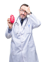 Wall Mural - Middle age senior hoary cardiologist doctor man holding heart over isolated background stressed with hand on head, shocked with shame and surprise face, angry and frustrated. Fear and upset.