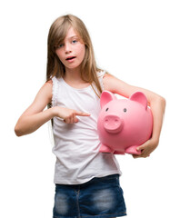 Poster - Young blonde toddler holding piggy bank very happy pointing with hand and finger