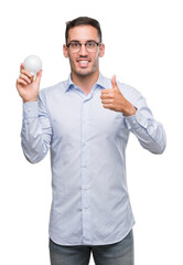 Sticker - Handsome young man holding lightbulb as idea happy with big smile doing ok sign, thumb up with fingers, excellent sign