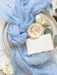 Card near light blue tulle fabric knot and cream roses on plates top view copy space, wedding mockup