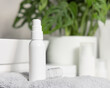 White one pump cosmetic bottle on grey folded towel near basin and green plant, mockup