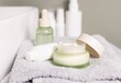 Opened green cream jar on grey folded bath towel close up,  cosmetic skincare product
