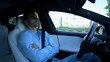 Male businessperson experience to ride an autonomous self driving electric car at urban road. Confident businessman resting during riding on electrical auto with autopilot at city. Slow motion